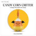 Illustration: the candy corn critter keychain hanging from its cord in front of a yellow circle