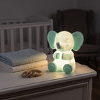 Illustration: the elephant night light glowing at night in a nursery on a dresser beside folded blankets