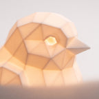 Illustration: close-up of the sparrow lamp's faceted head, beak and glowing eye